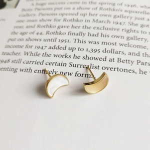 Macro shot of gold-plated moon earrings with white mother-of-pearl inlay on book