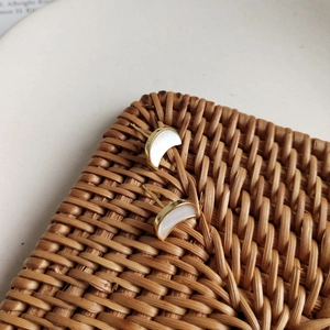 Detail of crescent moon shell stud earrings with gold plating on a textured rattan surface