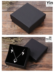 Gros plan d'un collier renard argenté dans une boîte cadeau en papier noir texturé