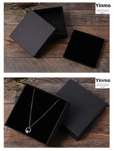 Détail d'une boîte à bijoux en papier kraft noir avec collier argenté sur fond de bois