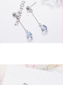 Macro detail of silver drop earring with iridescent cube crystal on white card