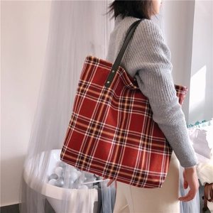 Detail of red plaid canvas tote bag with black leather handles and metal rivets