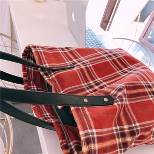 Detail view of thick red plaid tote bag with black leather straps and golden rivets