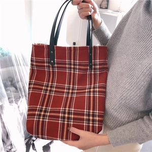 Macro detail of red plaid tote bag featuring textured fabric and durable leather handles