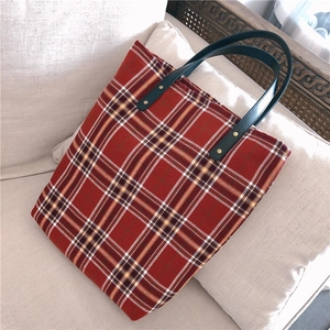 Detail of red and navy checkered tote bag featuring black leather handle and metal rivets