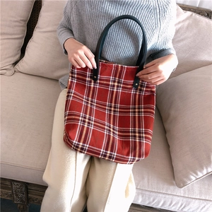 Detail of red and navy checkered tote bag featuring black leather handles and durable fabric