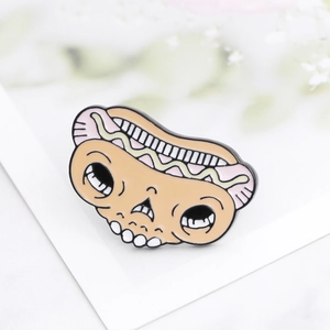 Detailed view of punk style enamel hot dog skull brooch on white backing card