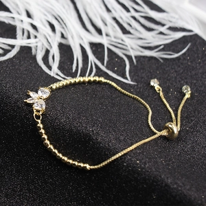 Detail of adjustable gold bracelet featuring a sparkling zircon butterfly charm on black background