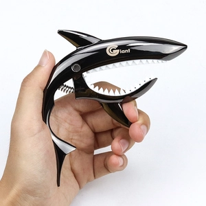 Black shark-shaped zinc alloy guitar capo held by hand on a clean white background