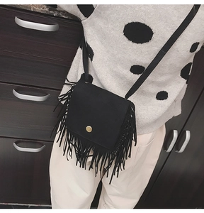 Black tassel crossbody bag with gold buckle shown on model to display size and drape