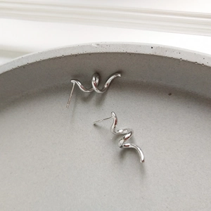 Close-up of S925 sterling silver spiral stud earrings on a gray minimalist tray