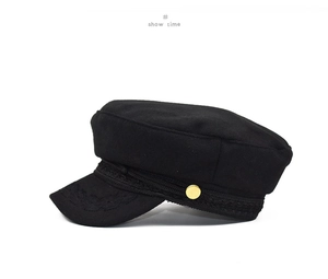 Detail of vintage wool baker boy hat featuring a black braided band and gold metal button