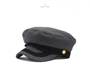 Detail of dark gray wool newsboy cap with black braided strap and gold button