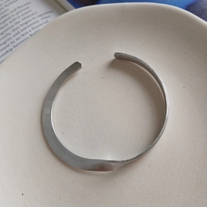 Vista macro del bracciale ritorto in argento opaco su vassoio beige e libri