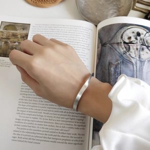 Dettaglio del bracciale ritorto in argento con trama opaca indossato su sfondo di libro