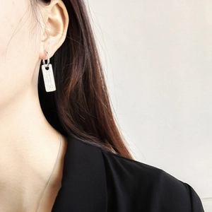 Close-up of minimalist silver rectangular tag earrings worn on model in black suit