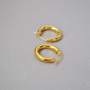 Close-up of golden chunky hoop earrings on textured grey fabric showing metal finish