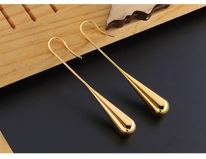 Macro view of golden waterdrop earrings on black reflective surface with wood detail