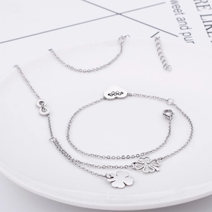 Elegant silver bracelet with heart, infinity, and clover charms on a white ceramic tray