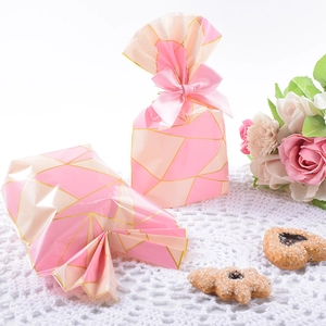 Elegant pink and gold geometric cookie bags with ribbons on a white lace backdrop