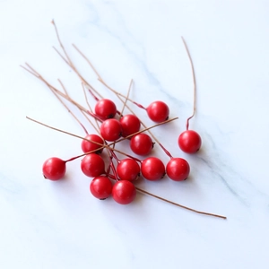 Artificial red berries on brown stems scattered on a marble surface for DIY decor