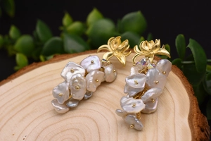 Dettaglio macro degli orecchini con perle barocche e fiori su sfondo in legno naturale
