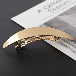 Minimalist golden oval metal hair clip with a brushed finish on a black background
