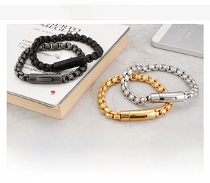 Detail of square box chain bracelets in gold, steel, and black on marble surface