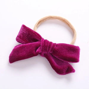 Detail of purple velvet bow attached to a beige elastic nylon headband for babies