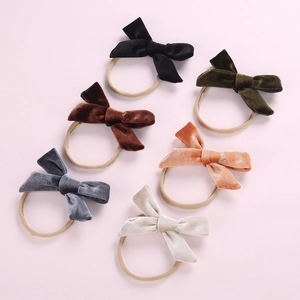 Flat lay of six colorful velvet bow nylon headbands for babies on a soft pink background