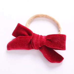 Close-up of red velvet baby bow with beige nylon headband on plain white background