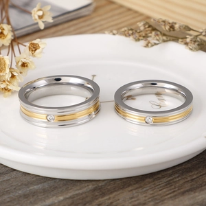Polished silver and gold titanium steel couple rings with central zircon in a ceramic dish