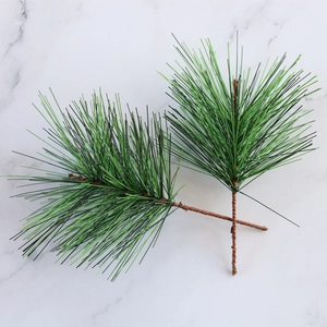 Close-up of artificial green PVC pine needles with brown wire stems on marble background