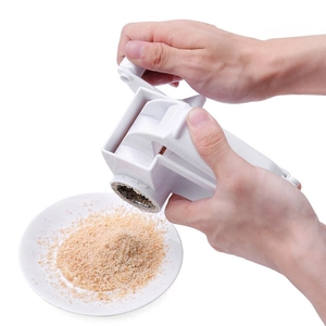 Manual stainless steel cheese grater with rotary handle grinding food into a white plate