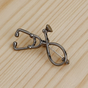 Detail of dark grey stethoscope brooch showing metallic texture and pin backing on wood