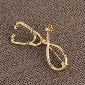 Detailed view of polished gold stethoscope brooch on dark textured fabric background