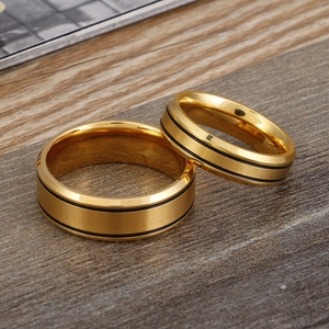 Brushed gold stainless steel couple rings with black inlay displayed on a wooden surface