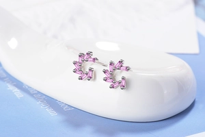 Detailed macro of silver pinwheel earrings with purple zircon on white ceramic stand