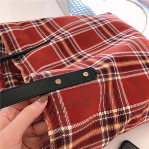 Detail of red plaid canvas tote bag with black leather handle and copper rivets