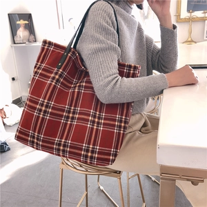 Macro detail of red and navy tartan canvas tote with leather straps and metal rivets