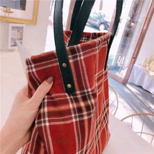 Detail view of red plaid tote bag with black leather handle and vintage metal rivets