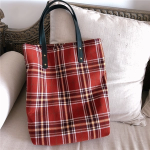 Detail of red plaid tote bag with dark green leather handles and gold rivet accents