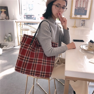 Detail of red plaid tote bag featuring slim black leather straps in a cafe setting