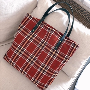 Detail of red plaid canvas tote bag showing textured fabric and leather handles