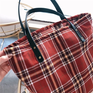 Detailed view of red plaid tote bag with black leather straps and gold rivets