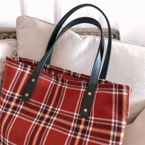Detail of red tartan tote bag with textured fabric, matte black straps and gold rivets