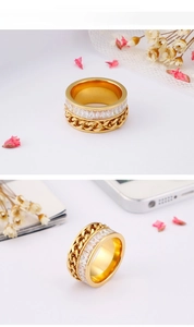 Close-up of golden ring with white zircon stones and Cuban chain links on white wood