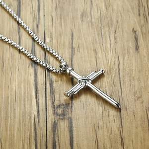 Detail shot of silver nail cross pendant with wire wrap on a rustic wooden surface