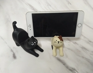 Close-up of cute resin cat phone stands in black and calico patterns on white marble
