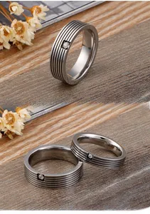 Close-up of silver titanium steel rings with parallel grooves and a small square diamond
